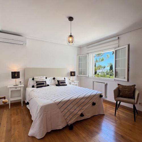 Un dormitorio blanco con una cama grande y una silla. en Villa Bloom, en Nuestra Señora de Jesús