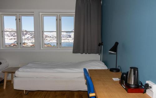 a bedroom with a bed and a table and windows at Hotel Angmagssalik in Tasiilaq