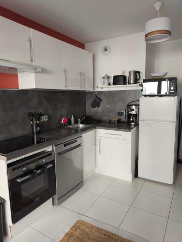 une cuisine avec des armoires blanches et des appareils noirs dans l'établissement Studio calme et paisible, climatisé avec terrasse au dernier étage, 100m du tramway et 20 min de la promenade des anglais, à Nice