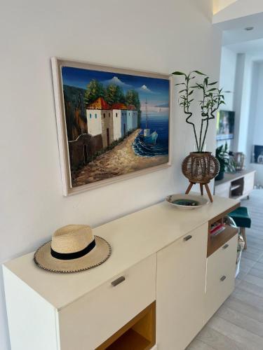 a white cabinet with a hat on it with a painting on the wall at Nea Peramos Apartment SeaFront in Néa Péramos