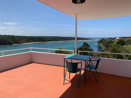 a balcony with a table and chairs and a view of the water at Casa no Rio - River House in Vila Nova de Milfontes