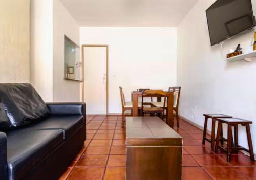a living room with a black leather couch and a table at Pé na areia, Prainha in Arraial do Cabo