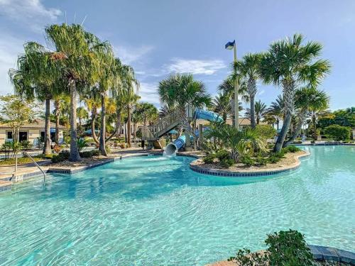 a large swimming pool with palm trees and a slide at Wonderful Disney-Themed Home in ChampionsGate Resort 15 min from Disney World with 7 pools, Club houses, Water Park, Gym, Arcades, Lazy River, Golf, and More! in Kissimmee