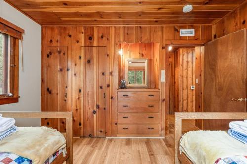 two beds in a bedroom with wooden walls and wooden floors at Cub House- Remodeled cabin INSIDE Yosemite with new hot tub and more in North Wawona