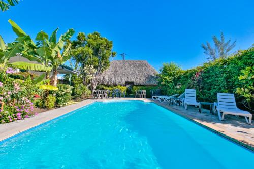 - une piscine dans un complexe avec des chaises et un toit de chaume dans l'établissement Pension De La Plage, à Punaauia