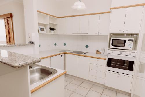 a white kitchen with a sink and a microwave at The Point Coolum in Coolum Beach