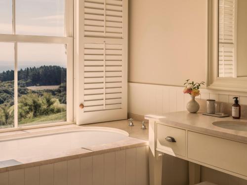 a white bathroom with a tub and a window at Rosewood Cape Kidnappers in Te Awanga