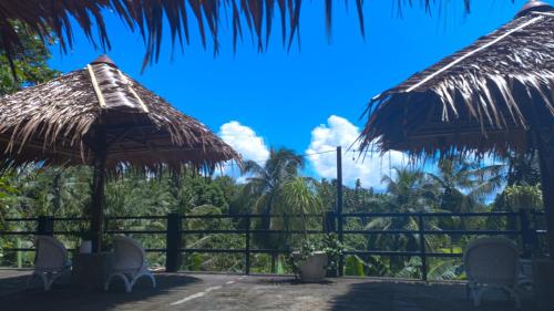 two straw umbrellas and chairs in front of a fence at Guesthouse Thalassa in Bunaken