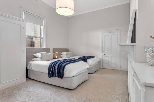 a white bedroom with two beds and a fireplace at Norfolk on the Esplanade - Steps to Grange Beach in Grange