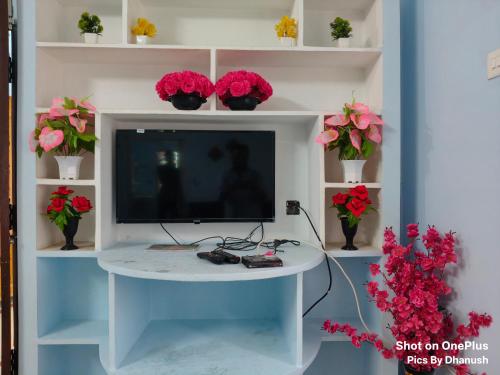 a tv sitting on a white shelf with flowers at Annamaiah Guest House & Homestay - Tirupati - Home Food Service in Tirupati