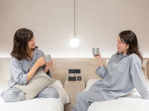 two women sitting on a bed holding up cups at HOTEL THE LEBEN OSAKA in Osaka