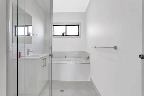 a white bathroom with a shower and a sink at Modern Coastal Retreat in Aldinga Beach Just Steps from the Shore in Aldinga Beach