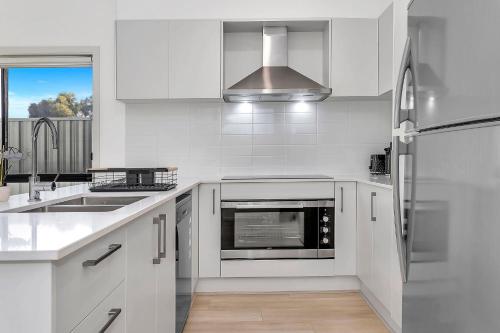 a white kitchen with a sink and a refrigerator at Modern Coastal Retreat in Aldinga Beach Just Steps from the Shore in Aldinga Beach