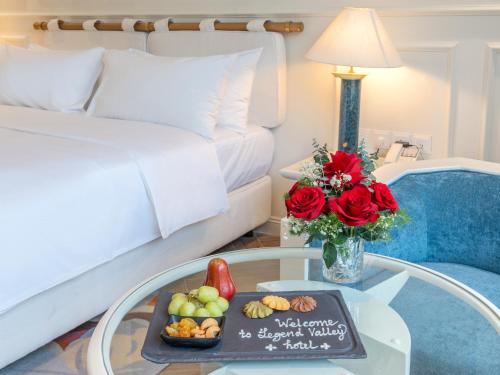 a room with a bed and a table with a tray of fruit at Legend Valley Hotel Ha Nam in Phủ Lý