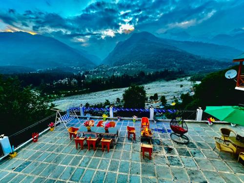 a patio with tables and chairs and a view of mountains at The Holly Woods Resort, Manali - Blissful View From Rooms in Manāli