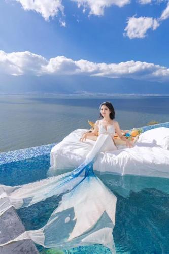 a woman in a white dress sitting on a bed in the water at Dali Mermaid Seascape Resort Hotel in Dali