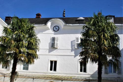a white building with a clock tower and two palm trees at Domaine AGERRIA in Mauléon-Licharre