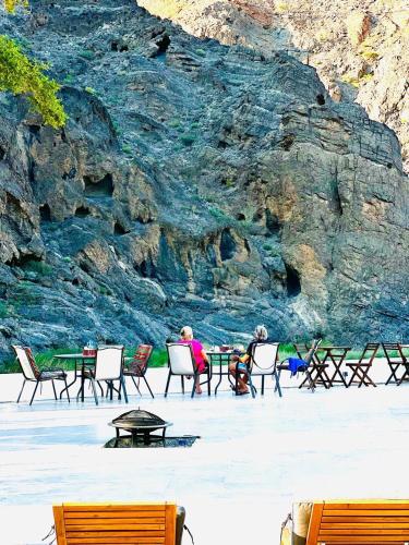 two people sitting at tables in chairs in front of a mountain at Wadi Al Arbeieen Resort in Muscat