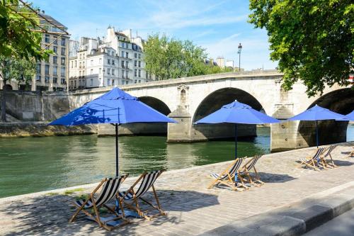 un groupe de chaises avec des parasols bleus à côté d'une rivière dans l'établissement Mini loft in Notre Dame district, Île Saint-Louis, Paris, à Paris