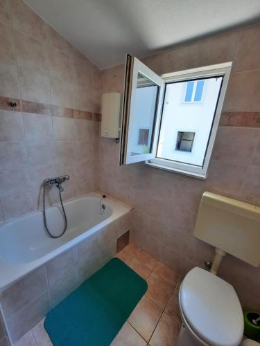a bathroom with a tub and a toilet and a window at Apartman Val in Rogoznica