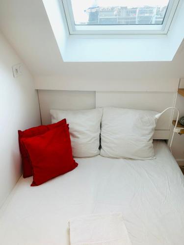 - un lit blanc avec un oreiller rouge dans l'établissement CENTRAL Paris Emplacement exceptionnel Nid coquet Tout EQUIPE salle de bains wc Vue Paris Climatisation Ascenseur, à Paris