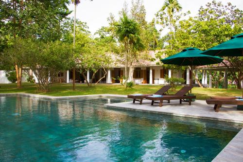 ein Pool mit Bänken und Sonnenschirmen neben einem Haus in der Unterkunft Boundary House in Galle