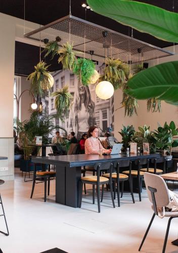 a woman sitting at a table in a restaurant with plants at Anne&Max Boutique Hotel in Utrecht