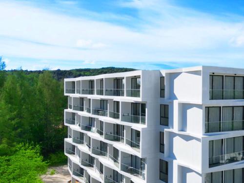 a white apartment building with trees in the background at Laya Suites and Residences in Bang Tao Beach