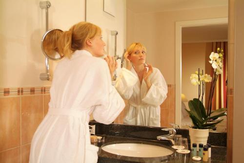 a woman standing in front of a bathroom mirror at Best Western Plus Hotel Erb in Parsdorf