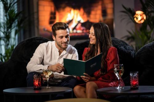 a man and a woman sitting on a couch with a book at Best Western Plus Hotel Erb in Parsdorf