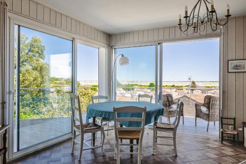 - une salle à manger avec une table, des chaises et de grandes fenêtres dans l'établissement Maison Bordure de Forêt et vue Mer, à Saint-Trojan-les-Bains