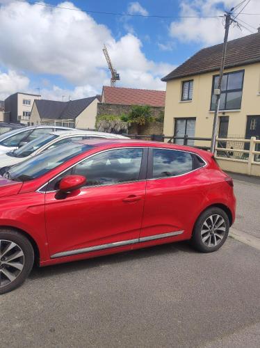 une voiture rouge garée à côté d'une rangée de voitures garées dans l'établissement Studio Carentan, à Carentan