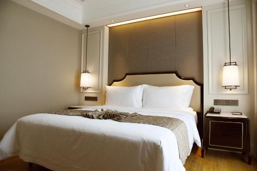 a bedroom with a large white bed with two lights at Ramada Plaza by Wyndham Wenzhou in Wenzhou