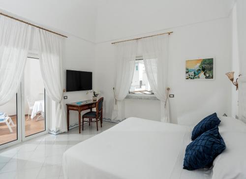 a white bedroom with a bed and a desk at Hotel Quisisana in Capri