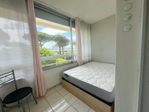 une chambre avec un lit et une fenêtre avec une chaise dans l'établissement Cocon au Grau-du-Roi Calme, lumineux, à 200m de la plage, au Grau-du-Roi