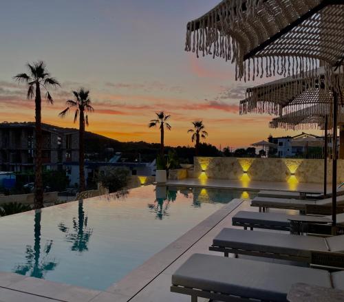 a swimming pool with chairs and palm trees at sunset at Asters Hotel in Ksamil
