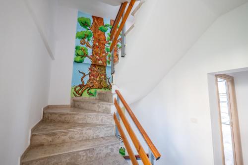 a staircase with a painting of a tree on the wall at Lazy Roo Hostel Saranda in Sarandë