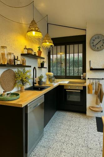 une cuisine avec des placards noirs, un évier et une horloge dans l'établissement Charmante maison rénovée à Arès, à Arès