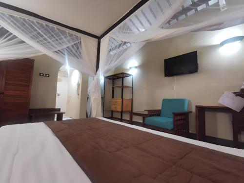 a bedroom with a bed and a chair and a tv at Hôtel de la Palmeraie in Bujumbura