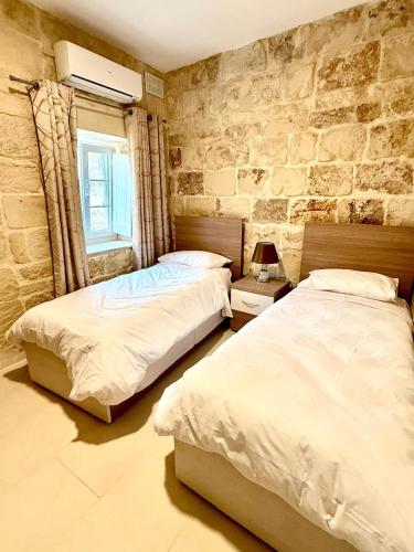 two beds in a bedroom with a stone wall at Charming 3-Bedroom House of Character - Perfect Family Retreat - Naxxar in Il-Gwejdi