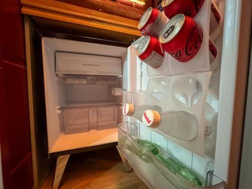 an open refrigerator with soda cans and bottles in it at Tucano - Deck Tiny House in Mairiporã