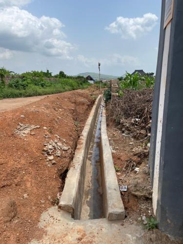 a drainage ditch on a dirt road next to a building at Umbrella Properties hotels and apartments - Moniya in Ibadan