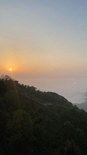 a sunset on a hill with trees and the sun at Hotel Nagarkot Inn in Nagarkot