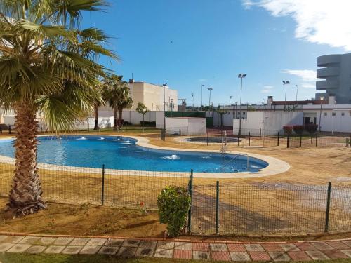 a swimming pool with a palm tree and a fence at Apartamento El Mirador del Cantil in Isla Cristina