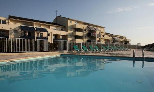 une piscine avec des chaises vertes et un bâtiment dans l'établissement Appartement sur Lacanau Bleu Marine, à Lacanau