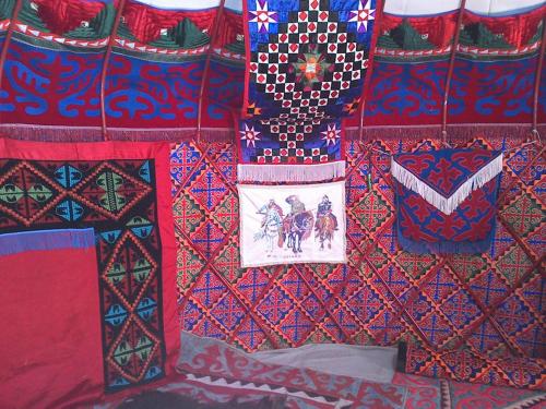 a wall covered in colorful blankets and pillows at Guest House Nur in Kochkor