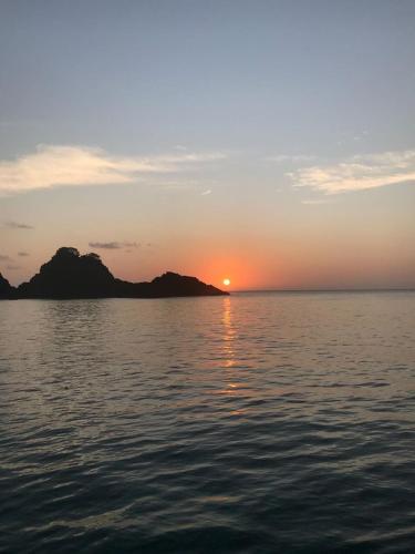 a sunset over a body of water with mountains at Villa Noronha Hostel e Suites in Fernando de Noronha