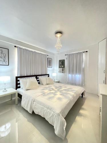 a white bedroom with a large bed and a chandelier at Your second home in Tagbilaran in Tagbilaran City