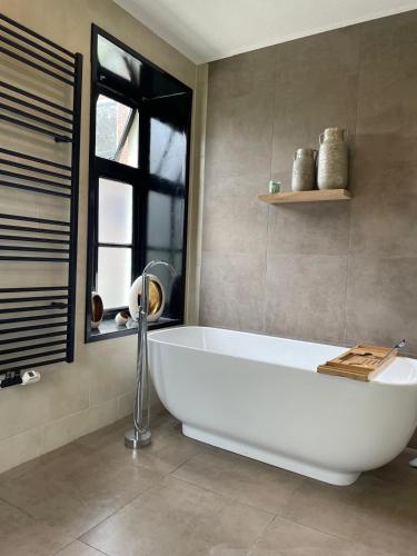 a white bath tub in a bathroom with a window at Slapen in een eeuwen oude Pastorie in Leermens
