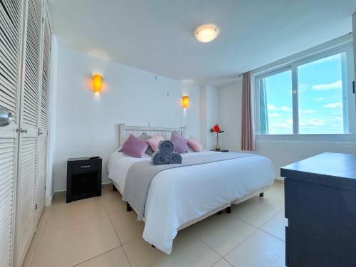 a white bedroom with a large bed with purple pillows at Paradisiaca Suite Cancun - BEACH CONDO - 4PX in Cancún